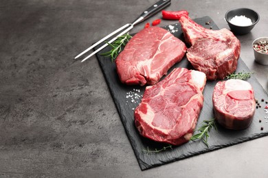 Photo of Pieces of raw beef meat, spices and carving fork on grey table, closeup. Space for text
