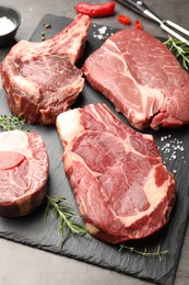 Photo of Pieces of raw beef meat, spices and carving fork on grey table, closeup