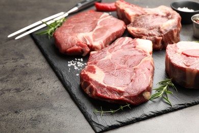 Photo of Pieces of raw beef meat, spices and carving fork on grey table, closeup. Space for text