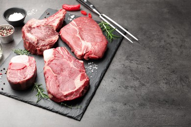 Photo of Pieces of raw beef meat, spices and carving fork on grey table, closeup. Space for text