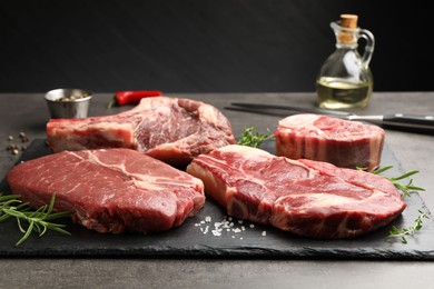 Photo of Pieces of raw beef meat and spices on grey table, closeup