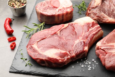 Photo of Pieces of raw beef meat and spices on grey table, closeup