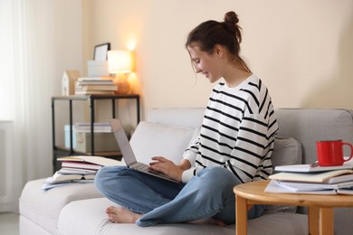 Photo of Smiling student with laptop preparing for exam on sofa at home