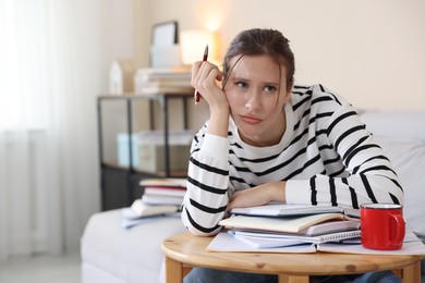 Photo of Worried student at table with books and mug preparing for exam on sofa indoors. Space for text