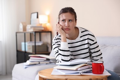 Photo of Worried student at table with books and mug preparing for exam on sofa indoors. Space for text