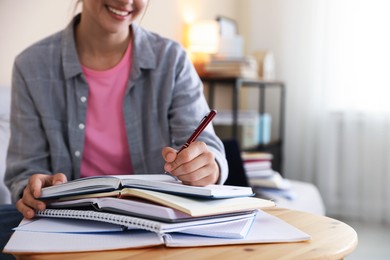 Photo of Smiling student with books and pen preparing for exam at wooden table indoors, closeup. Space for text