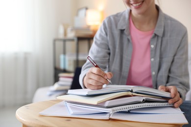 Photo of Smiling student with books and pen preparing for exam at wooden table indoors, closeup. Space for text