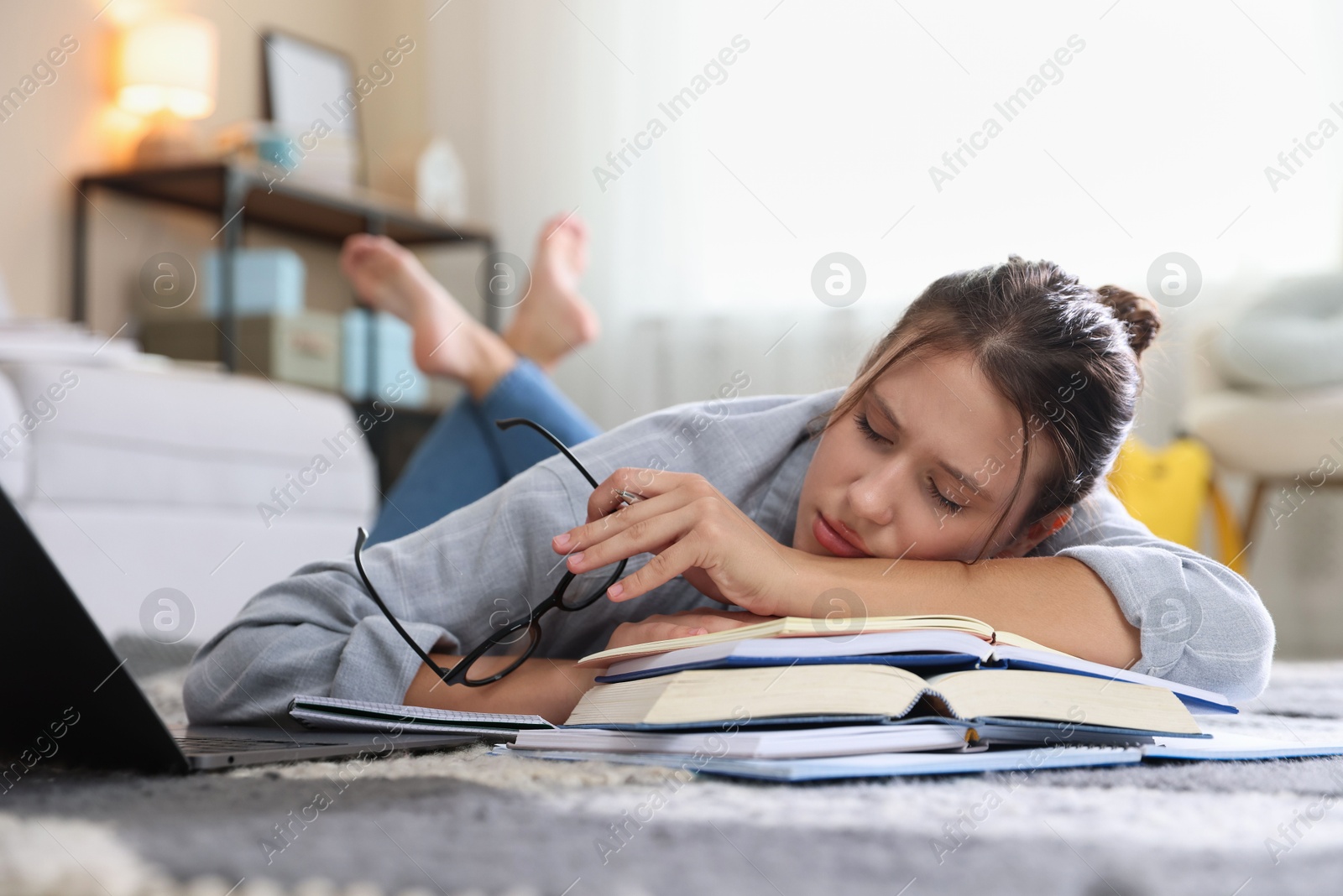 Photo of Tired student with glasses, laptop and books falling asleep before exam on floor indoors