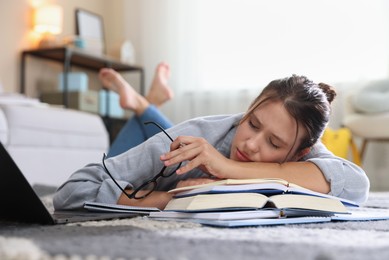 Photo of Tired student with glasses, laptop and books falling asleep before exam on floor indoors