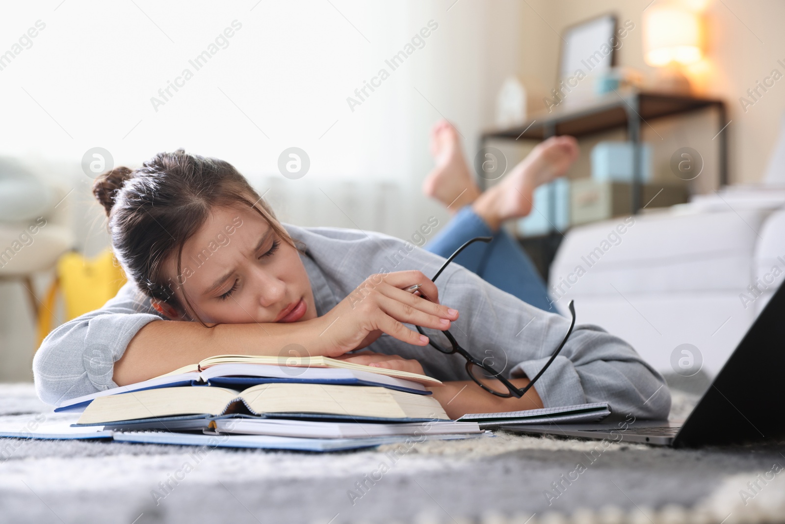 Photo of Tired student with glasses, laptop and books falling asleep before exam on floor indoors