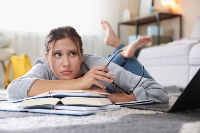 Photo of Worried student with glasses, laptop and books before exam on floor indoors