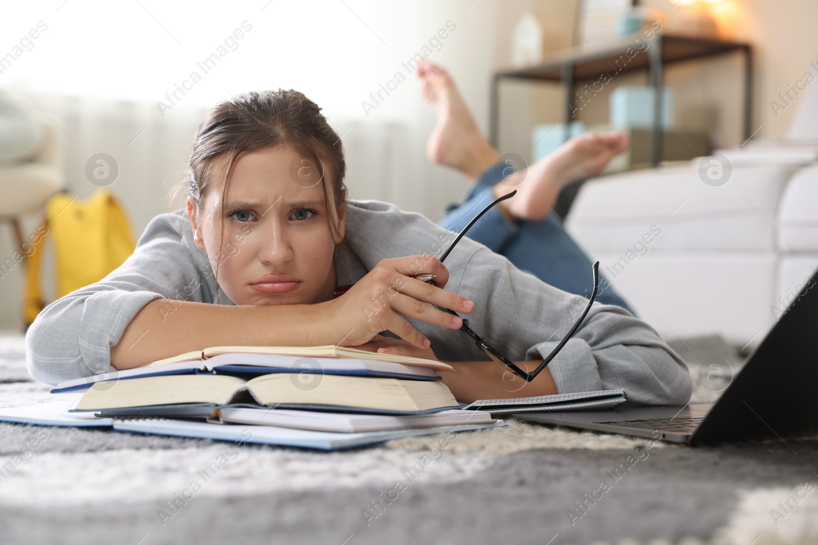 Photo of Worried student with glasses, laptop and books before exam on floor indoors