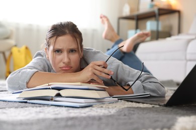 Photo of Worried student with glasses, laptop and books before exam on floor indoors