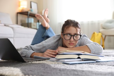 Photo of Worried student in glasses with laptop and books before exam on floor indoors