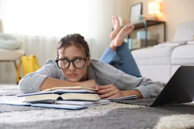 Photo of Worried student in glasses with laptop and books before exam on floor indoors