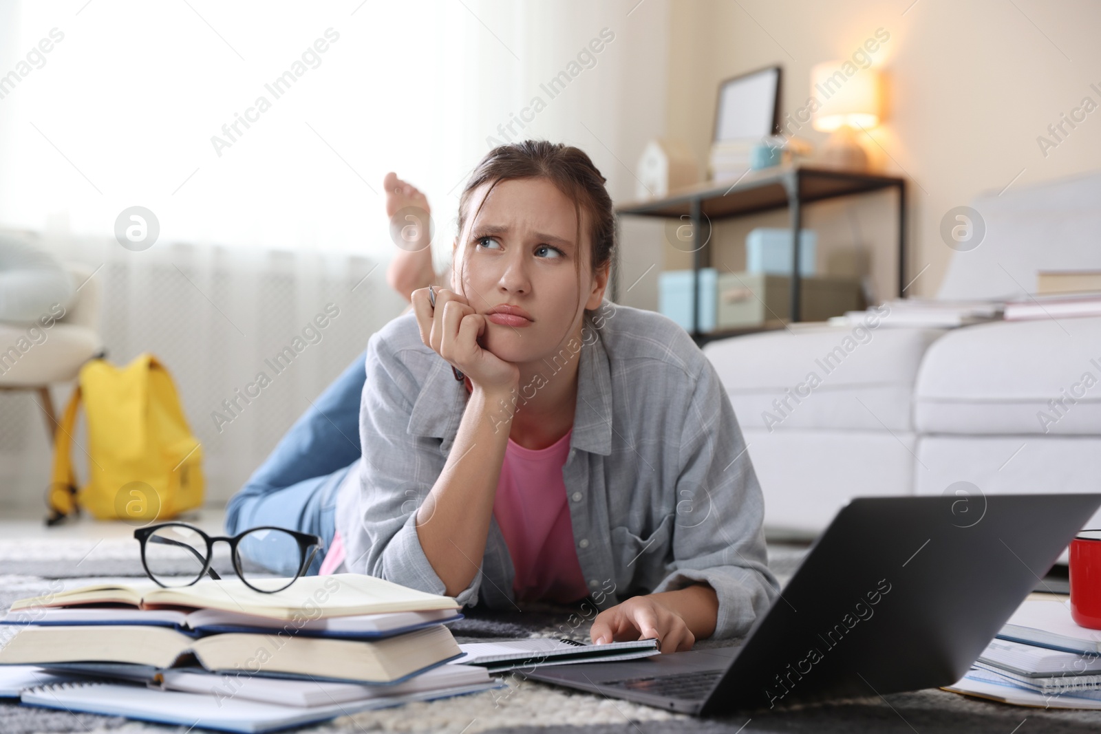 Photo of Worried student with laptop, books and pen preparing for exam on floor indoors