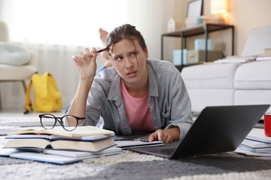 Photo of Worried student with laptop, books and pen preparing for exam on floor indoors