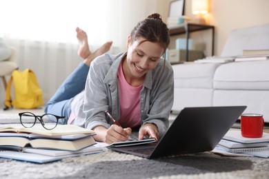 Photo of Smiling student with laptop, books and pen preparing for exam on floor indoors