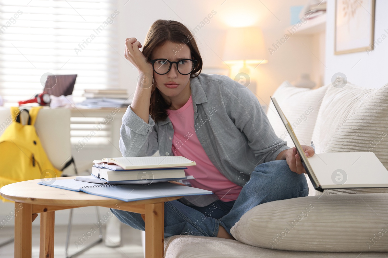 Photo of Worried student with books preparing for exam on sofa at home