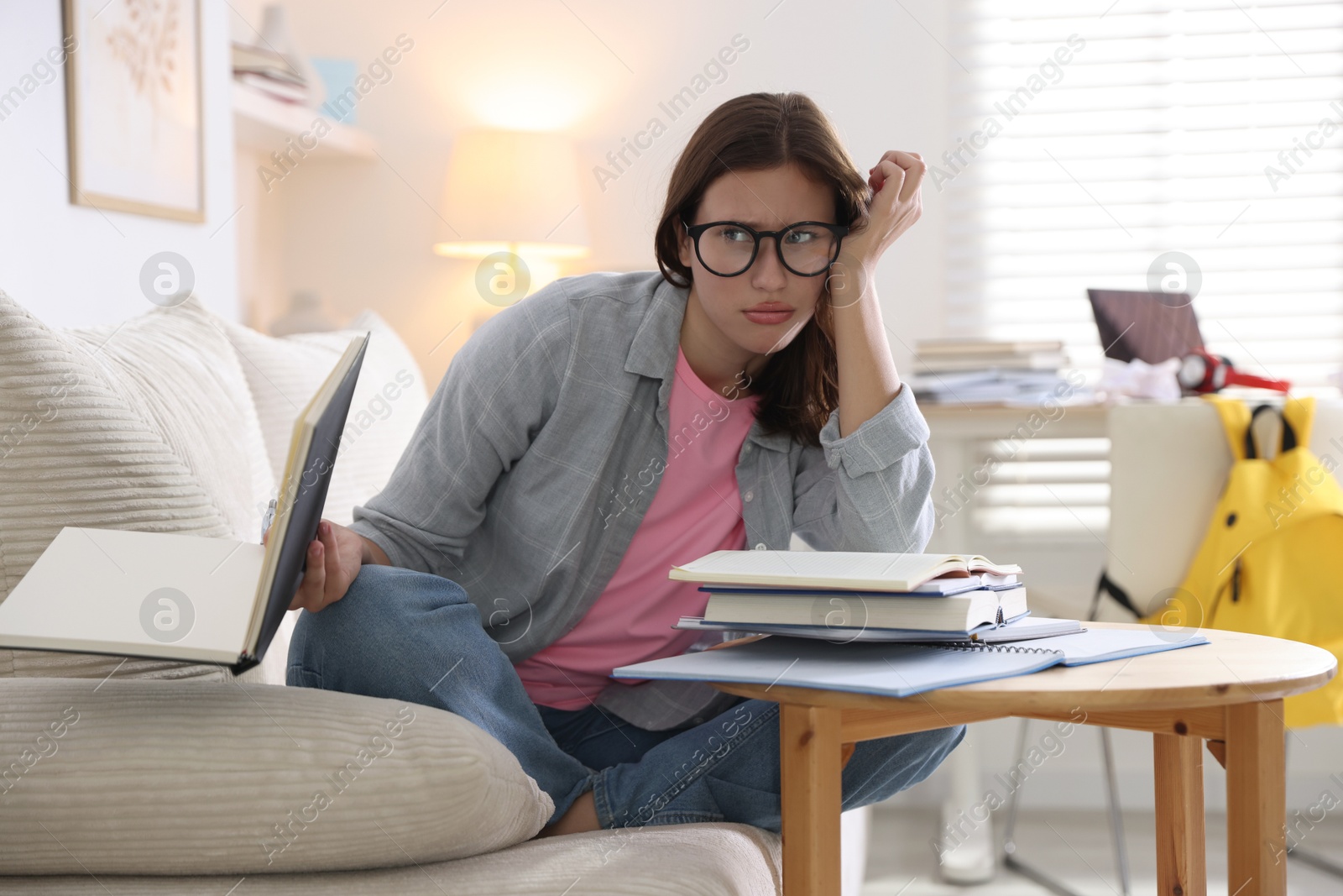 Photo of Worried student with books preparing for exam on sofa at home