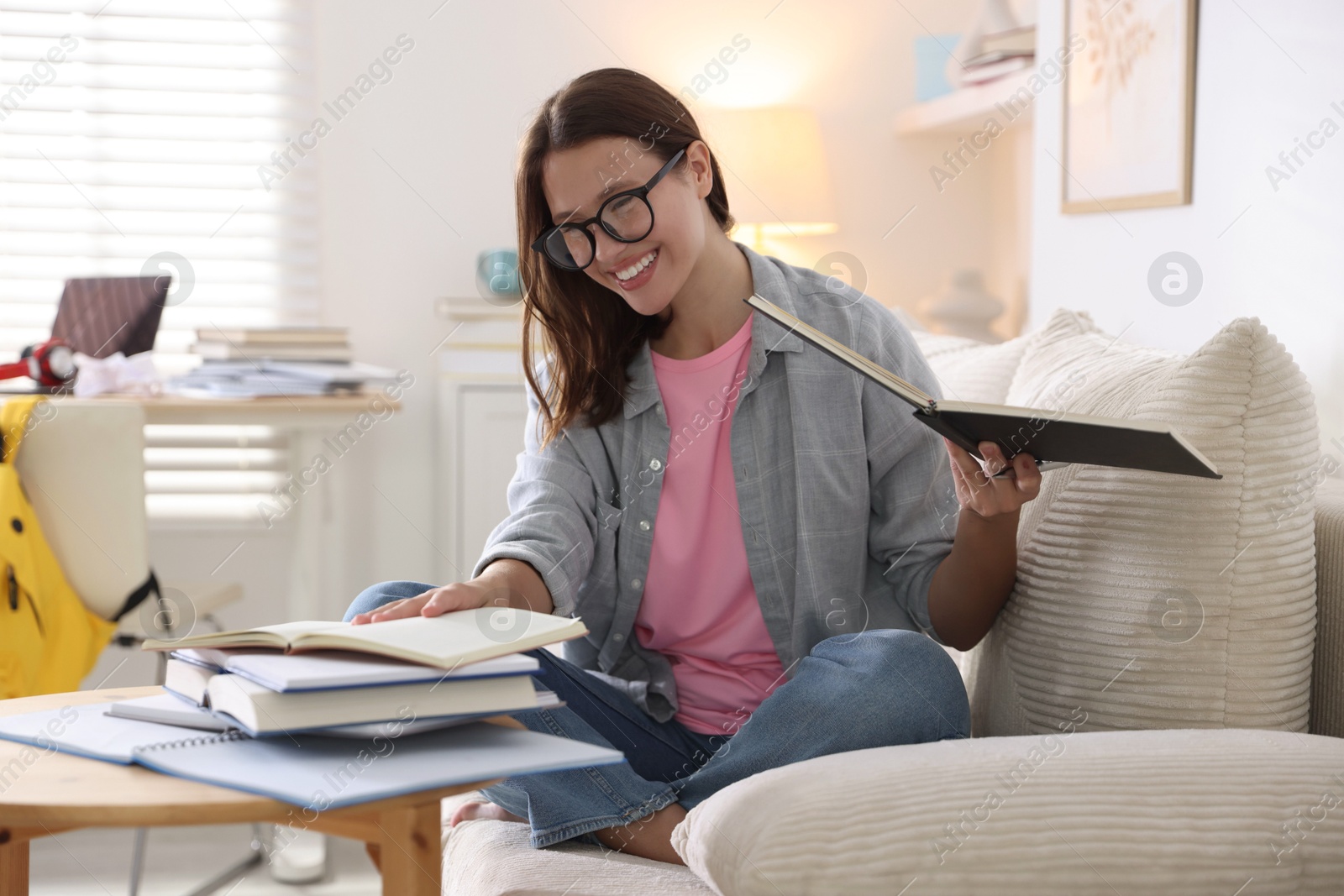 Photo of Smiling student with books preparing for exam on sofa at home