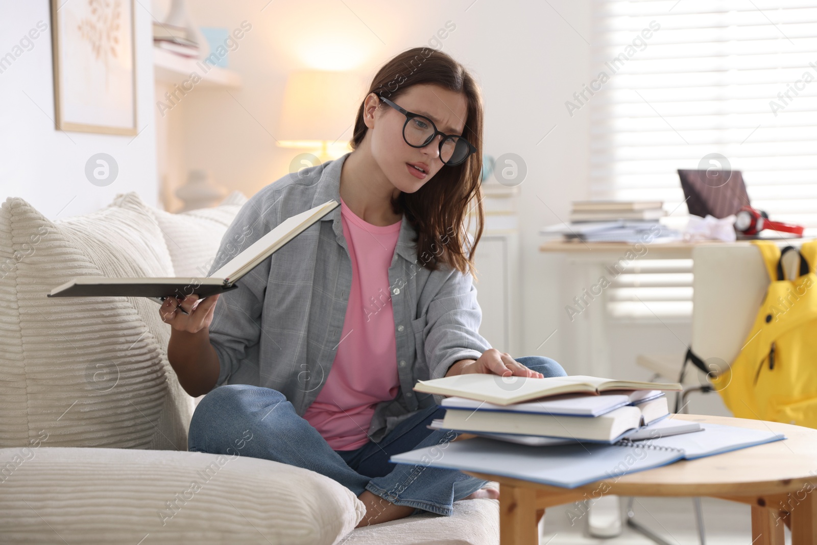 Photo of Worried student with books preparing for exam on sofa at home