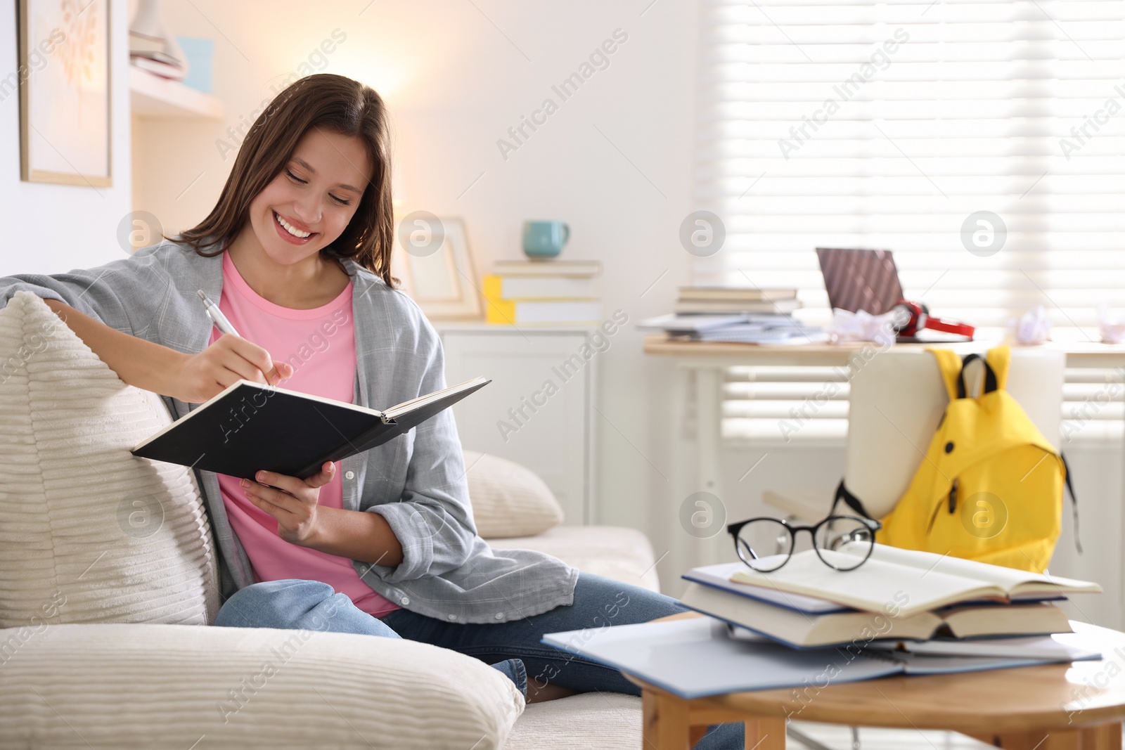 Photo of Smiling student with notebook and pen preparing for exam on sofa at home. Space for text