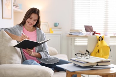 Photo of Smiling student with notebook and pen preparing for exam on sofa at home. Space for text
