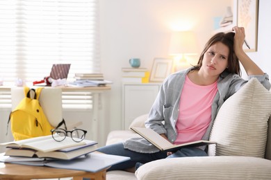 Photo of Tired student with book preparing for exam on sofa at home. Space for text