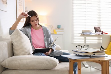 Photo of Tired student with book preparing for exam on sofa at home. Space for text