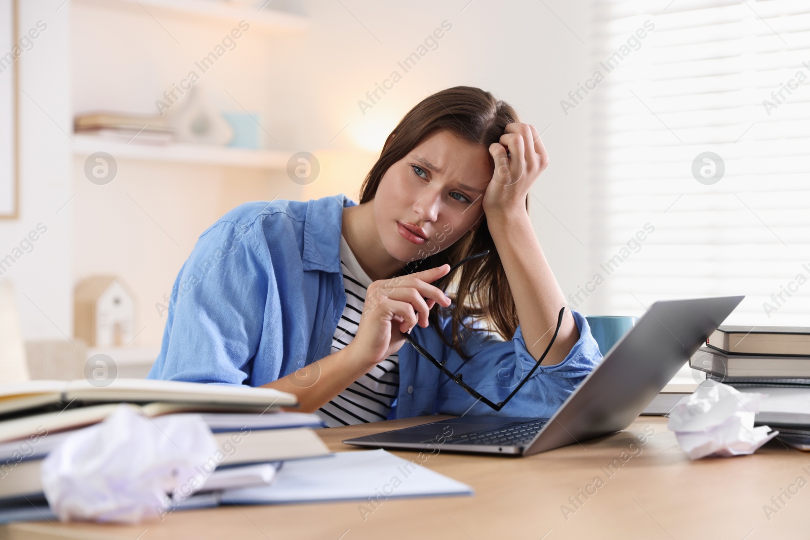 Photo of Worried student with glasses, laptop and books preparing for exam at table indoors
