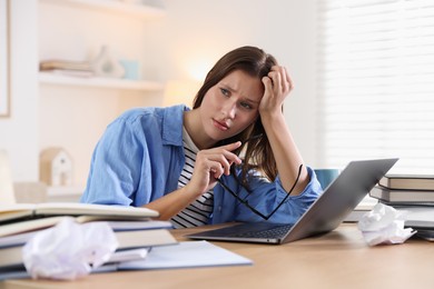 Photo of Worried student with glasses, laptop and books preparing for exam at table indoors