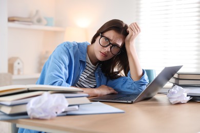 Photo of Worried student in glasses with laptop and books preparing for exam at table indoors