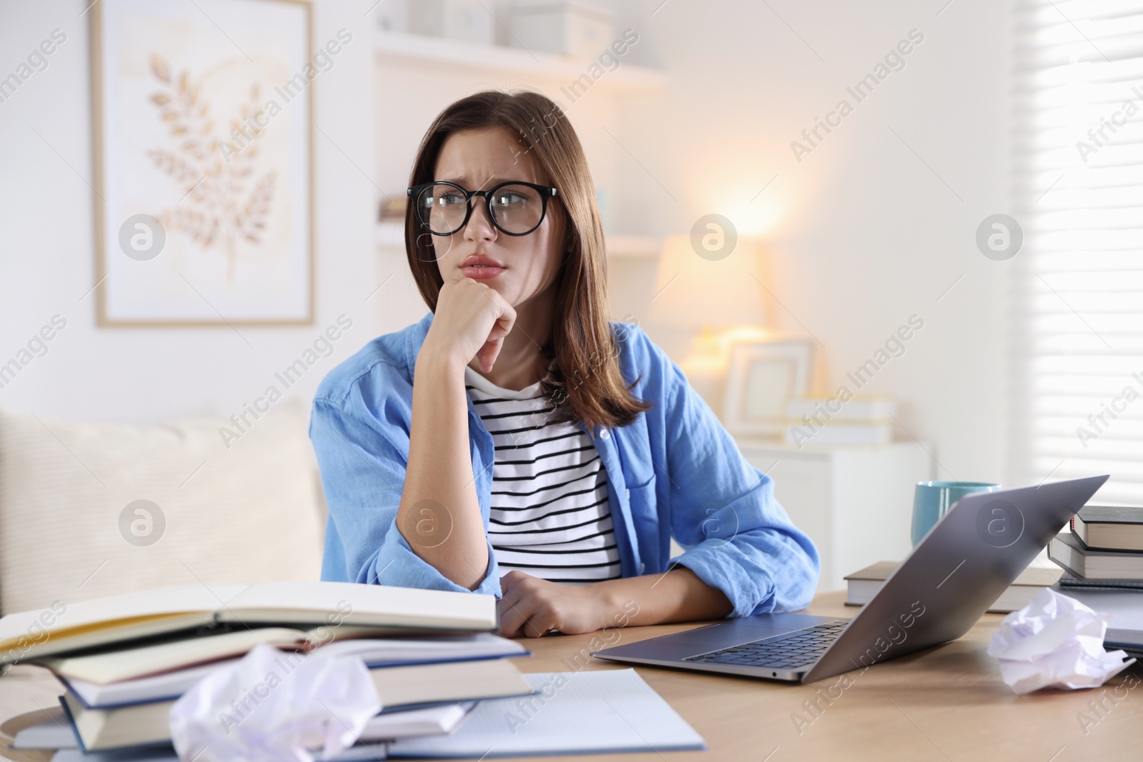Photo of Worried student in glasses with laptop and books preparing for exam at table indoors