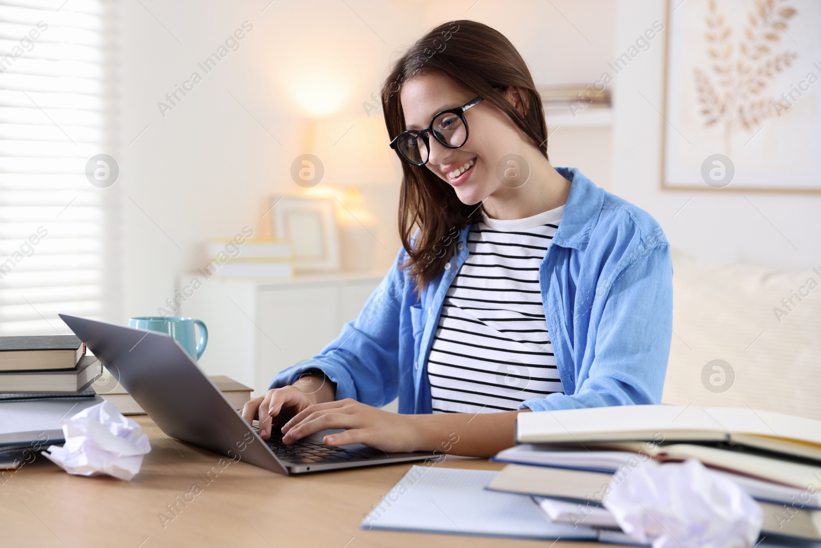 Photo of Smiling student in glasses with laptop and books preparing for exam at table indoors