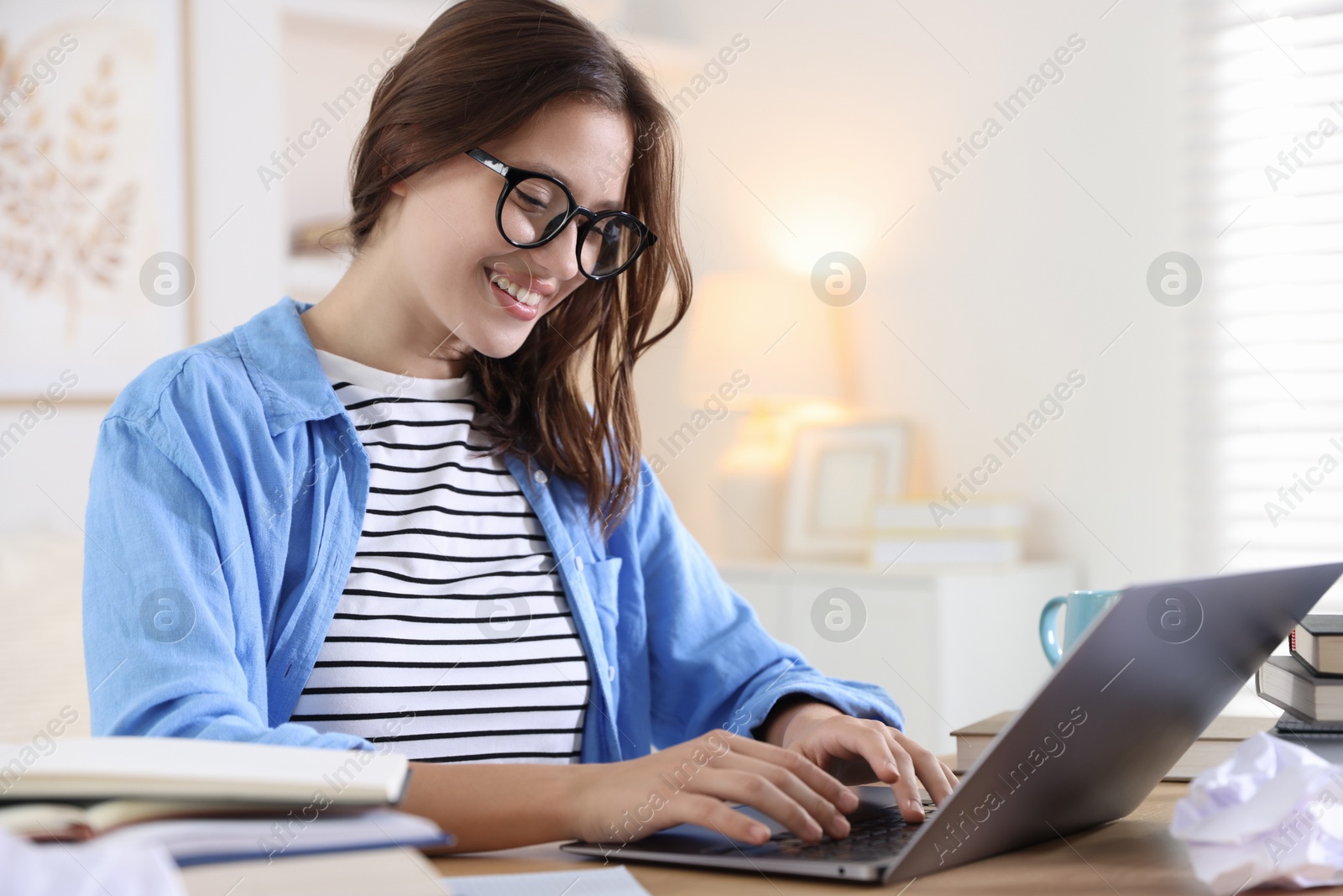 Photo of Smiling student in glasses with laptop and books preparing for exam at table indoors