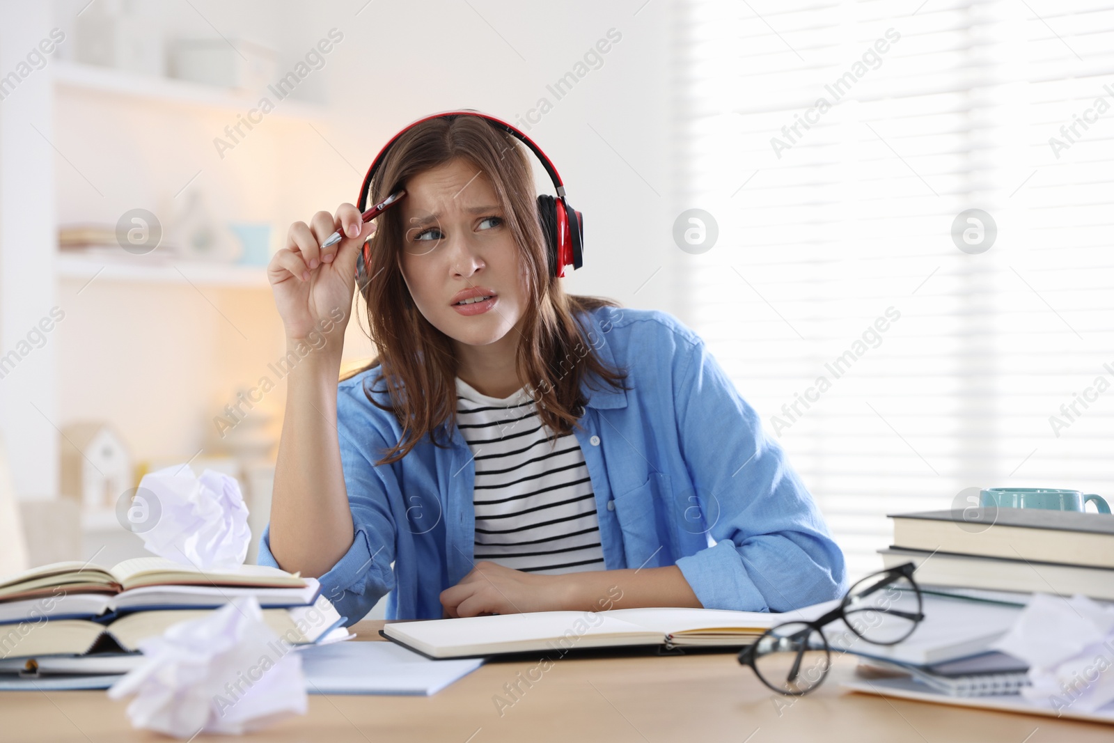 Photo of Tired student in headphones with pen and books preparing for exam at table indoors