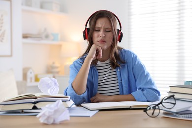 Photo of Tired student in headphones with books preparing for exam at table indoors