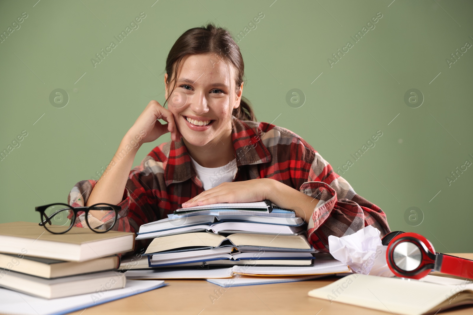 Photo of Portrait of smiling student with books preparing for exam at table near green wall