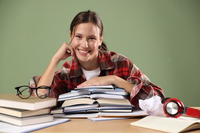 Photo of Portrait of smiling student with books preparing for exam at table near green wall
