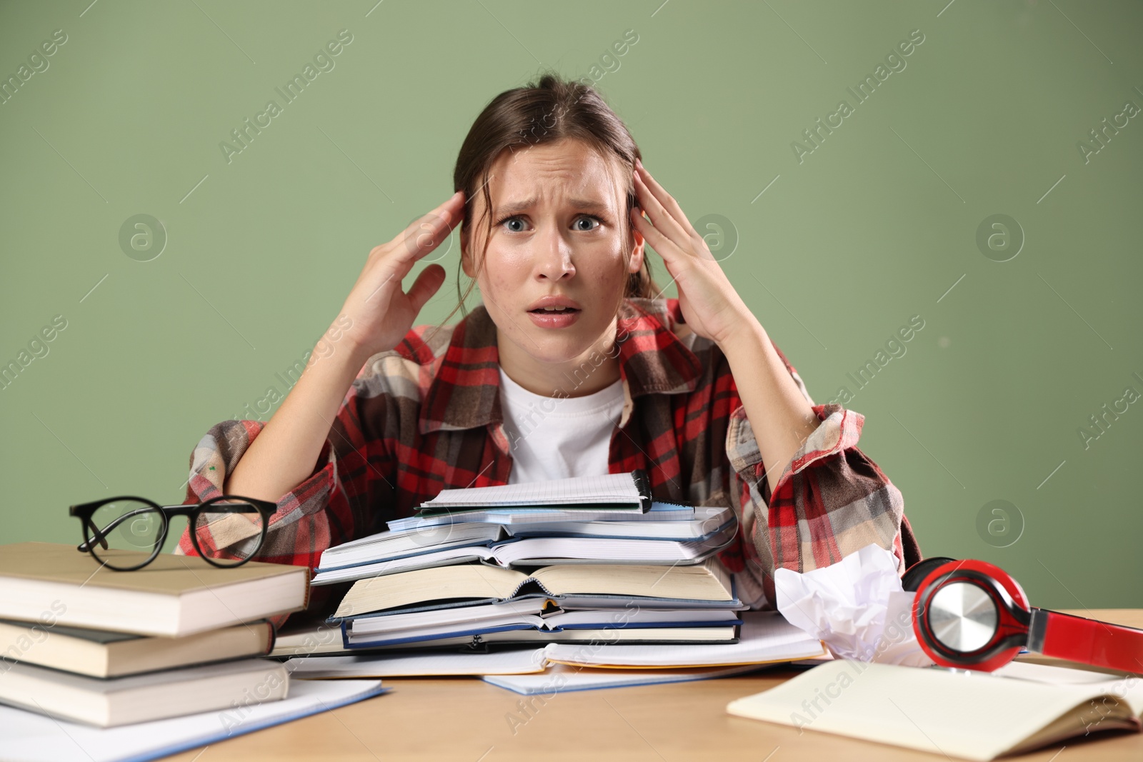 Photo of Worried student with books preparing for exam at table near green wall