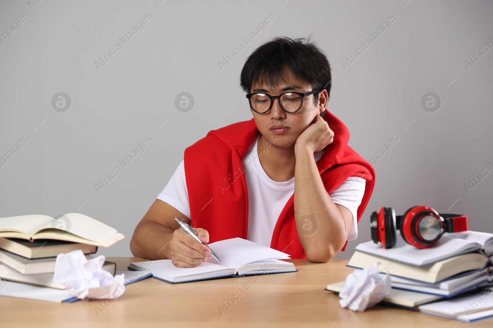 Photo of Student with pen and books preparing for exam at wooden table near grey wall