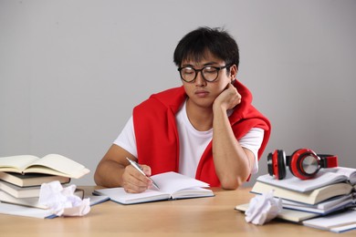 Photo of Student with pen and books preparing for exam at wooden table near grey wall