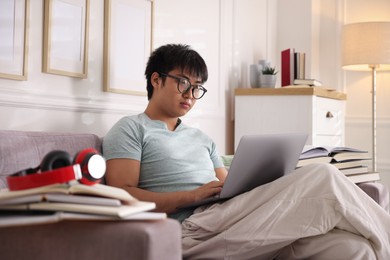 Photo of Student in glasses with laptop and books preparing for exam on sofa at home