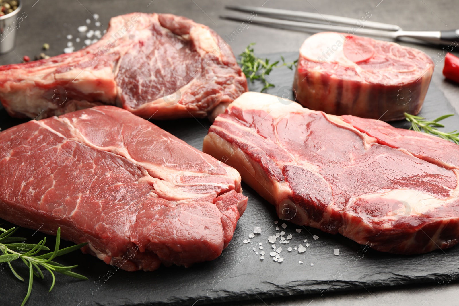 Pieces of raw beef meat, spices and carving fork on grey table, closeup Photo of Pieces of raw beef meat, spices and carving fork on grey table, closeup