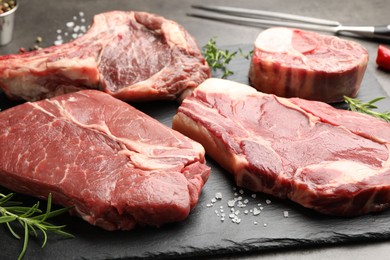 Photo of Pieces of raw beef meat, spices and carving fork on grey table, closeup