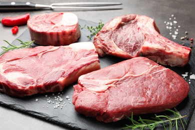 Photo of Pieces of raw beef meat, spices and carving fork on grey table, closeup