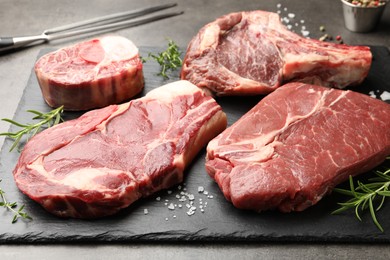 Photo of Pieces of raw beef meat, spices and carving fork on grey table, closeup