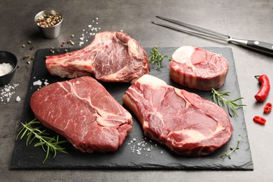 Photo of Pieces of raw beef meat, spices and carving fork on grey table, closeup