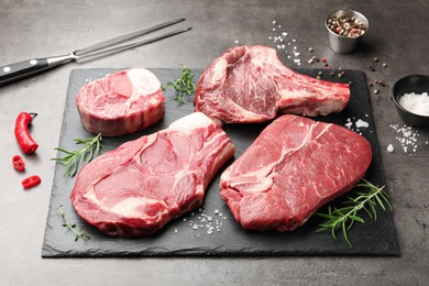 Photo of Pieces of raw beef meat, spices and carving fork on grey table, closeup